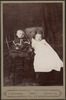Two infants, one in dark dotted dress the other in long christening gown